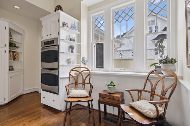 living area with dark wood-style flooring, wainscoting, and built in features