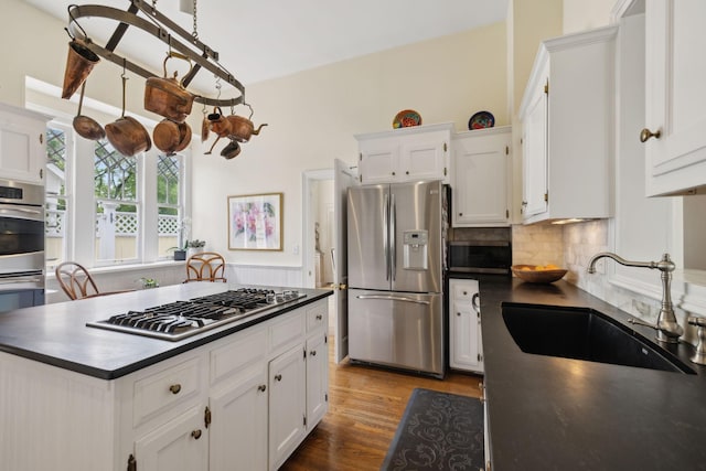 kitchen featuring dark countertops, white cabinets, a sink, appliances with stainless steel finishes, and backsplash