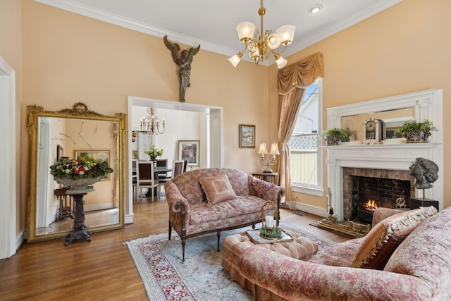 living room with an inviting chandelier, crown molding, wood finished floors, baseboards, and a warm lit fireplace