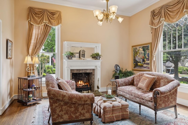 sitting room featuring a lit fireplace, wood finished floors, baseboards, an inviting chandelier, and ornamental molding
