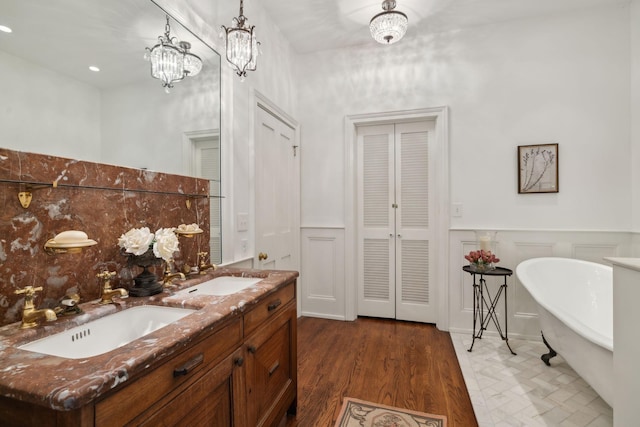 bathroom featuring double vanity, a soaking tub, a sink, and a wainscoted wall