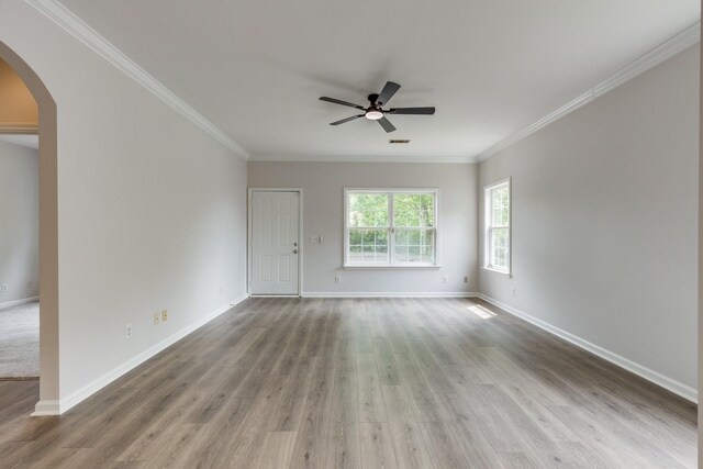 unfurnished room featuring crown molding, wood finished floors, baseboards, ceiling fan, and arched walkways