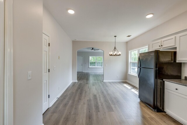 kitchen with freestanding refrigerator, light wood finished floors, arched walkways, and white cabinetry