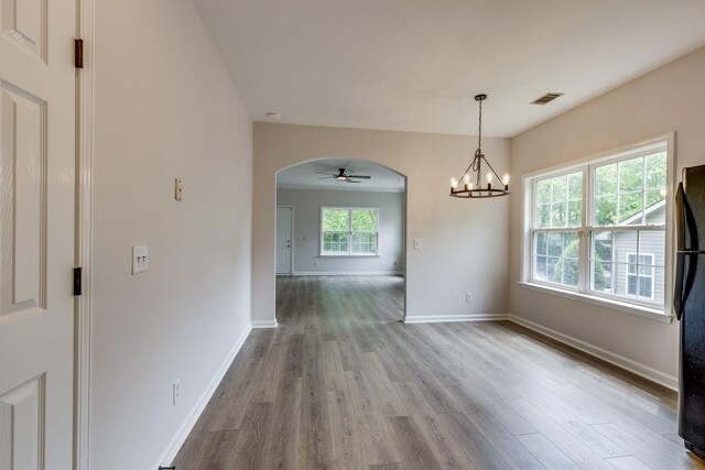 unfurnished dining area with visible vents, arched walkways, wood finished floors, baseboards, and ceiling fan with notable chandelier