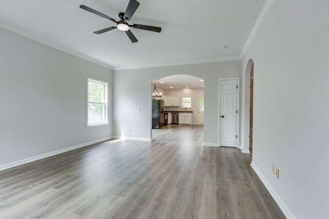 unfurnished living room featuring a ceiling fan, crown molding, arched walkways, wood finished floors, and baseboards