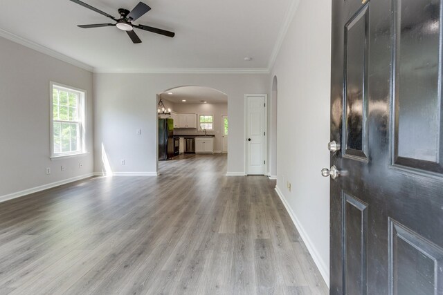 entrance foyer with crown molding, arched walkways, a ceiling fan, and light wood-type flooring