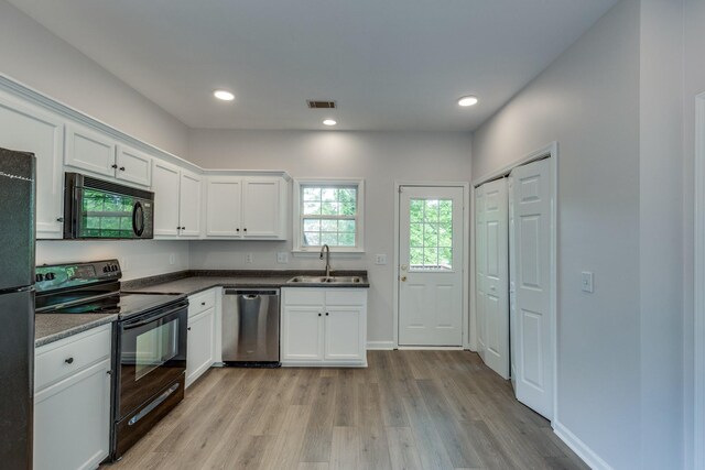 kitchen with a sink, light wood-style floors, white cabinetry, visible vents, and black appliances