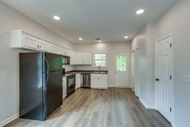 kitchen with dark countertops, light wood-type flooring, a sink, black appliances, and white cabinetry