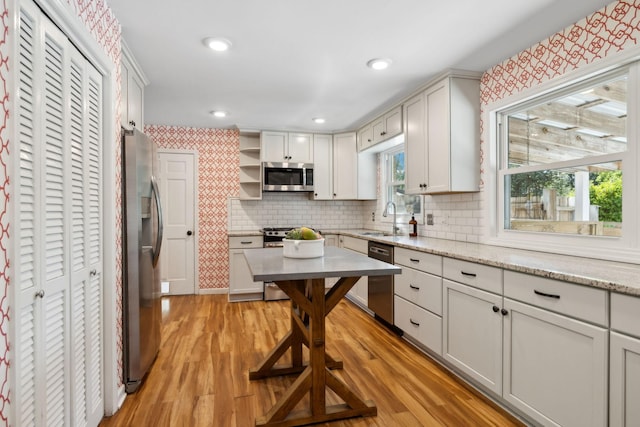 kitchen with open shelves, appliances with stainless steel finishes, a sink, light wood finished floors, and backsplash