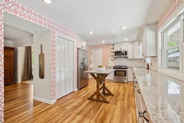 kitchen featuring appliances with stainless steel finishes, open shelves, a sink, baseboards, and light wood finished floors