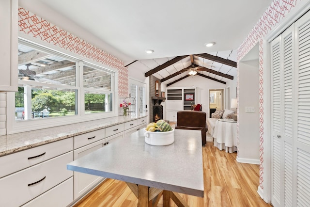 kitchen featuring a ceiling fan, white cabinets, light stone counters, lofted ceiling with beams, and light wood finished floors