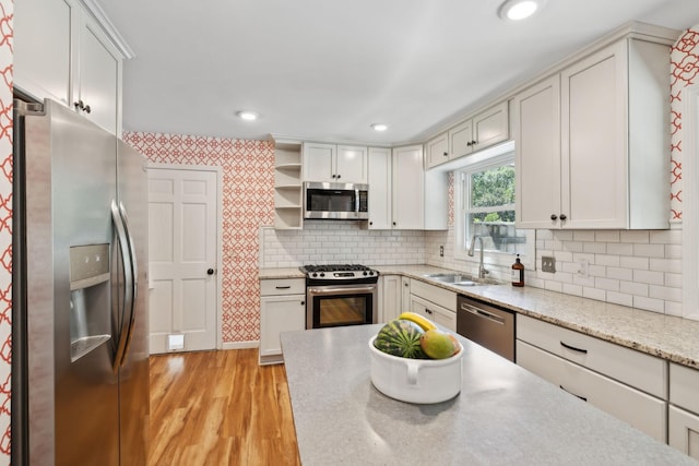 kitchen featuring backsplash, open shelves, a sink, stainless steel appliances, and light wood-style flooring