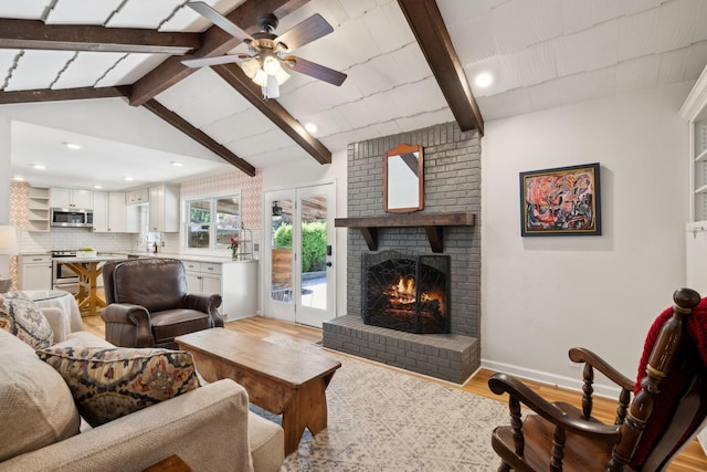 living area featuring ceiling fan, a fireplace, baseboards, vaulted ceiling with beams, and light wood-type flooring
