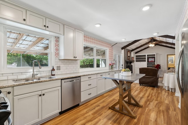 kitchen with appliances with stainless steel finishes, lofted ceiling with beams, a sink, light wood-style flooring, and backsplash