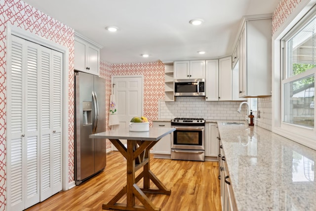kitchen featuring open shelves, wallpapered walls, light stone counters, a sink, and stainless steel appliances