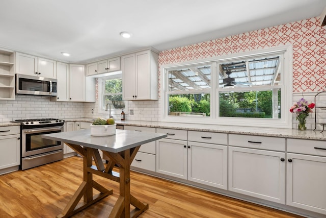 kitchen with open shelves, light wood-style floors, wallpapered walls, tasteful backsplash, and appliances with stainless steel finishes