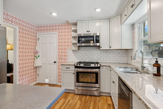 kitchen with a sink, appliances with stainless steel finishes, light wood-style floors, and wallpapered walls