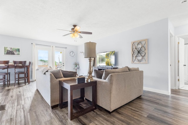living area featuring baseboards, a ceiling fan, a textured ceiling, and wood finished floors