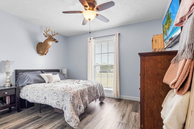 bedroom with a textured ceiling, baseboards, a ceiling fan, and wood finished floors