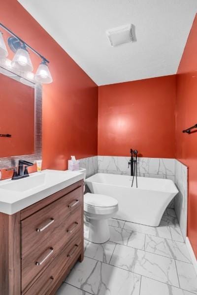 full bathroom with toilet, a soaking tub, marble finish floor, and vanity