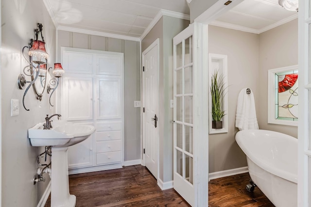 bathroom featuring crown molding, a freestanding tub, wood finished floors, a sink, and baseboards