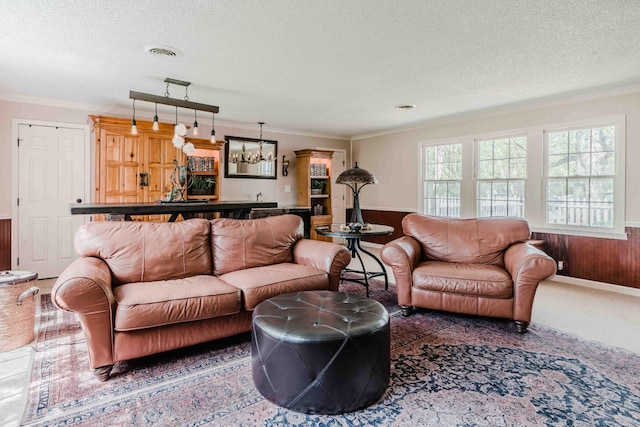 living room featuring wainscoting, a textured ceiling, a chandelier, visible vents, and ornamental molding