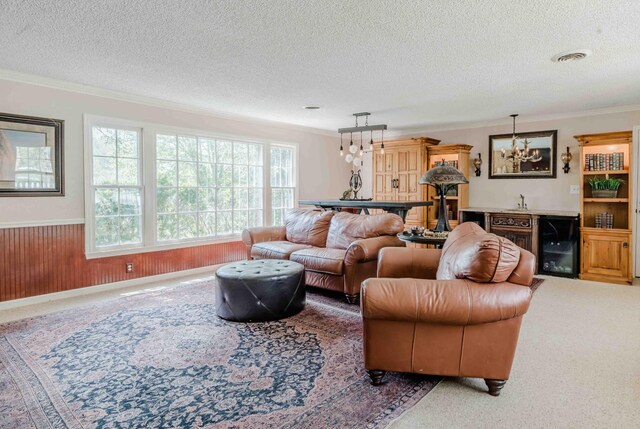 carpeted living room with a textured ceiling, crown molding, wainscoting, beverage cooler, and an inviting chandelier