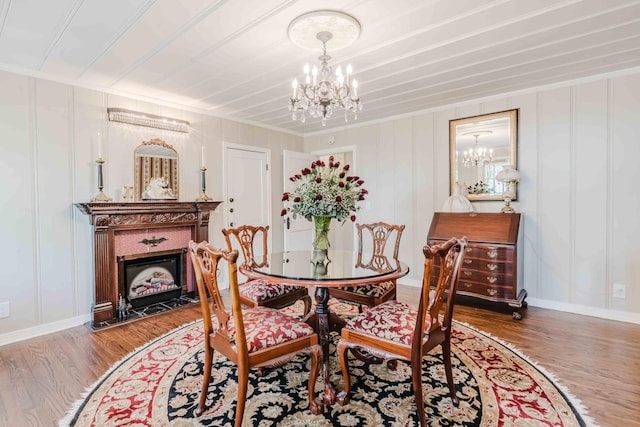 dining area with crown molding, a fireplace with flush hearth, wood finished floors, baseboards, and a notable chandelier
