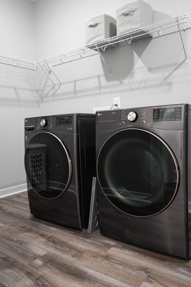 clothes washing area with independent washer and dryer, laundry area, baseboards, and wood finished floors