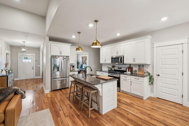 kitchen with a kitchen bar, light wood-type flooring, a sink, white cabinets, and stainless steel appliances
