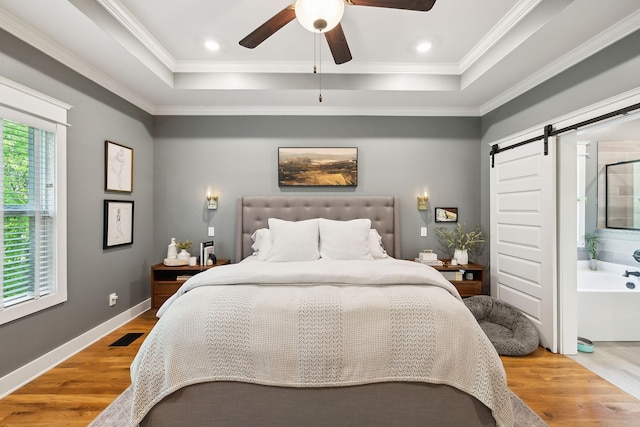 bedroom featuring crown molding, visible vents, wood finished floors, a barn door, and a tray ceiling