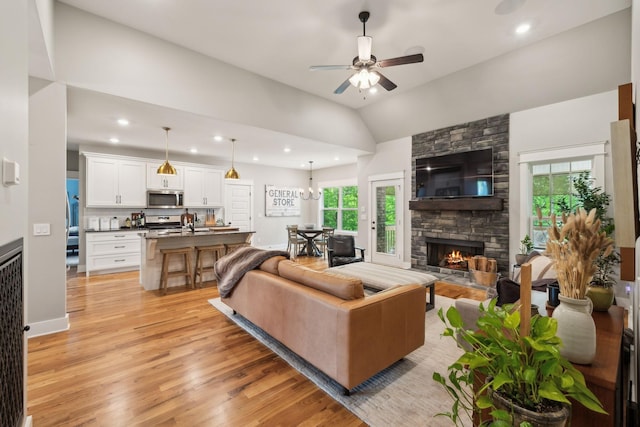 living area with ceiling fan, a stone fireplace, a healthy amount of sunlight, and light wood-type flooring