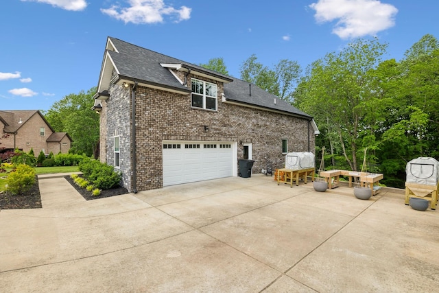 view of side of home featuring brick siding, a shingled roof, an attached garage, and driveway
