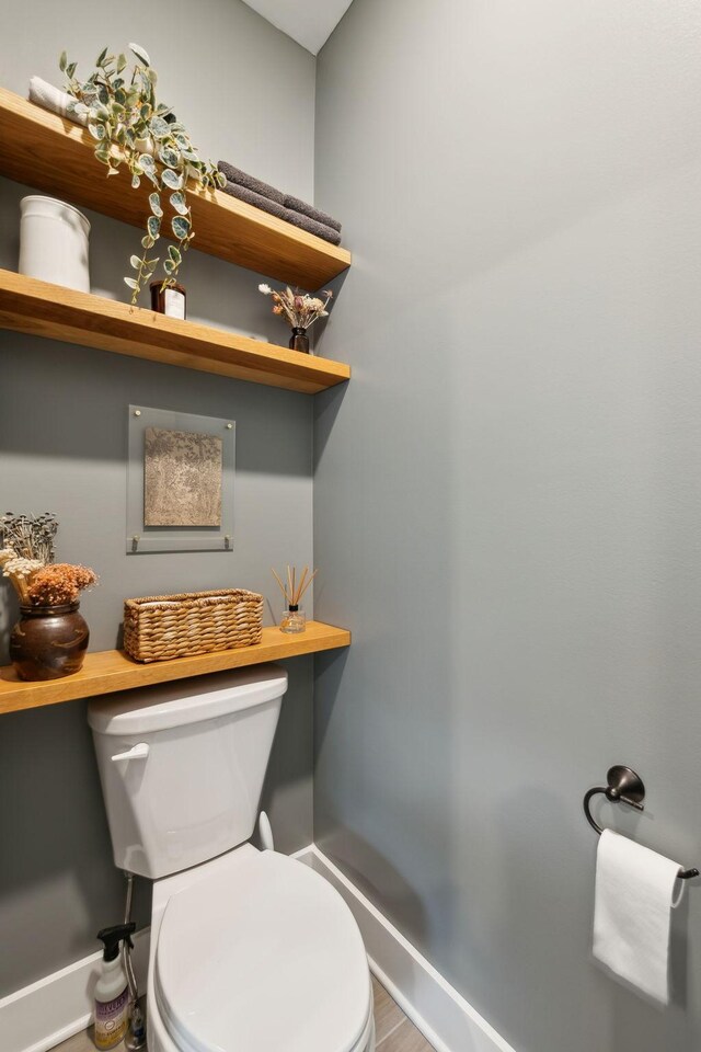 bathroom featuring baseboards, wood finished floors, and toilet