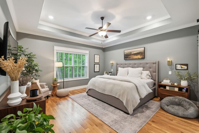 bedroom featuring ornamental molding, a raised ceiling, a ceiling fan, and wood finished floors