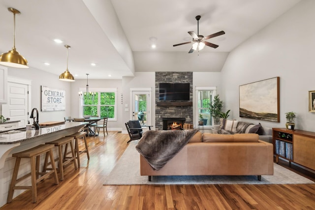 living room featuring lofted ceiling, a stone fireplace, recessed lighting, a ceiling fan, and light wood-style flooring