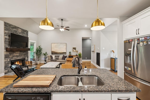kitchen with a fireplace, open floor plan, dark stone counters, stainless steel fridge with ice dispenser, and a sink