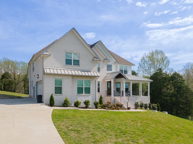 view of front facade with a standing seam roof, driveway, a garage, brick siding, and a front lawn