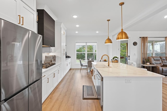 kitchen featuring appliances with stainless steel finishes, a center island with sink, light wood-type flooring, a sink, and white cabinets