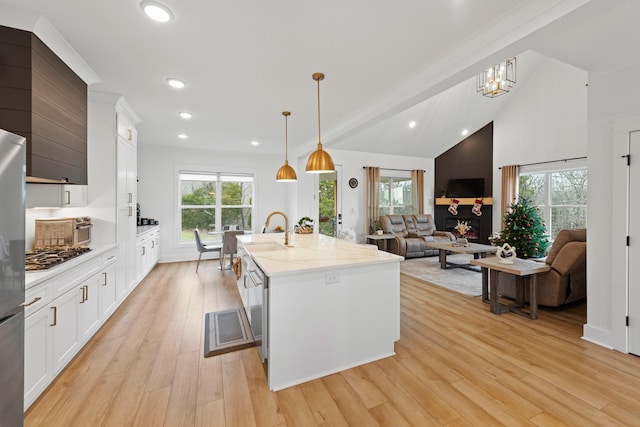 kitchen with light wood finished floors, a notable chandelier, white cabinets, and a center island with sink