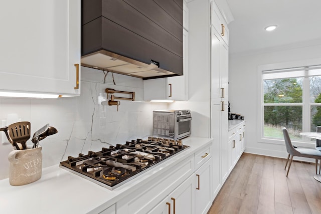 kitchen with tasteful backsplash, light countertops, stainless steel gas stovetop, custom range hood, and white cabinetry