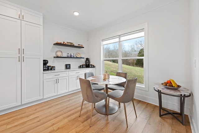 dining room featuring crown molding, a healthy amount of sunlight, a bar, and light wood finished floors