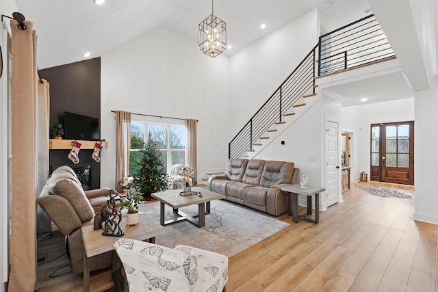 living room featuring a healthy amount of sunlight, high vaulted ceiling, light wood finished floors, and a chandelier