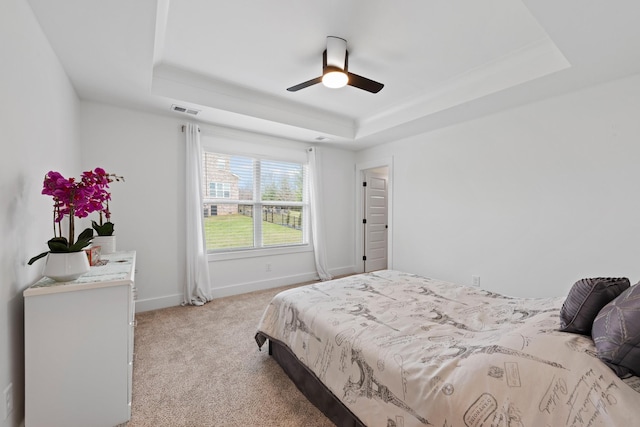bedroom with visible vents, light carpet, baseboards, a tray ceiling, and a ceiling fan