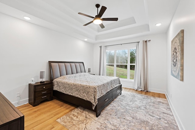 bedroom featuring light wood-type flooring, baseboards, ceiling fan, and a tray ceiling