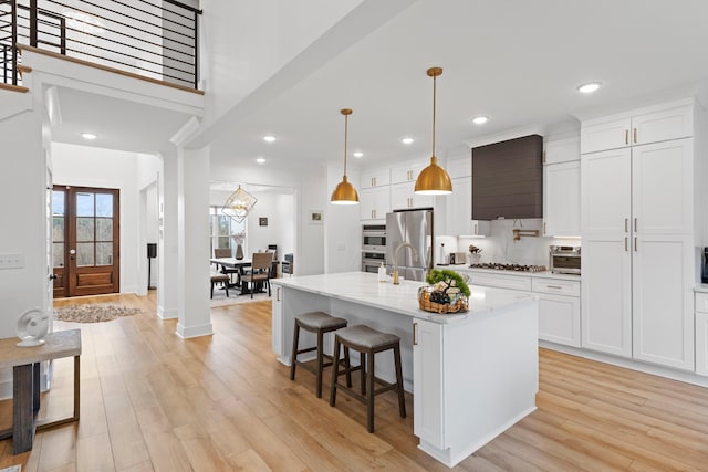 kitchen featuring freestanding refrigerator, a kitchen breakfast bar, a center island with sink, light wood-type flooring, and white cabinets