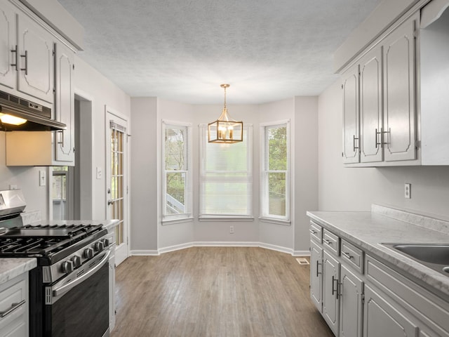 kitchen with stainless steel range with gas stovetop, light countertops, a notable chandelier, light wood-style floors, and under cabinet range hood