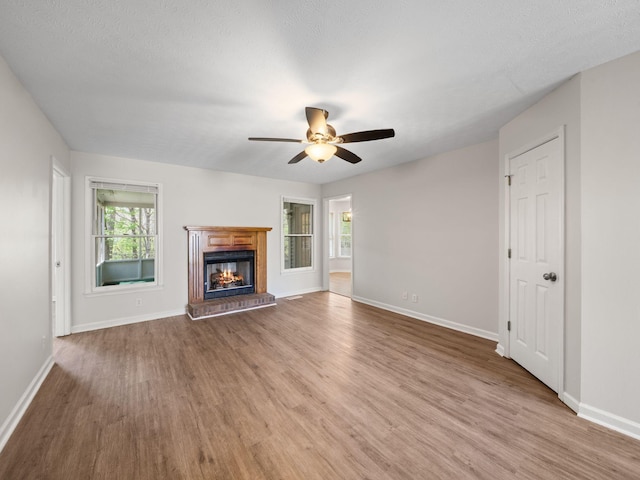 unfurnished living room with baseboards, a ceiling fan, a brick fireplace, and wood finished floors