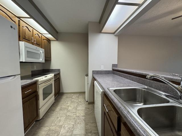 kitchen featuring stone finish flooring, a textured ceiling, dark countertops, a sink, and white appliances