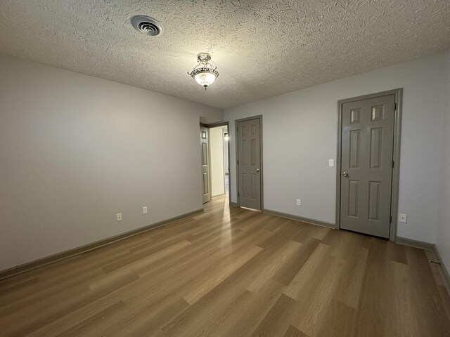 unfurnished room with baseboards, a textured ceiling, visible vents, and light wood-style flooring